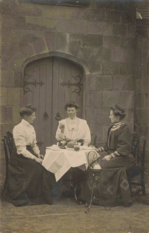 Old real photo postcard showing three ladies having a tea party