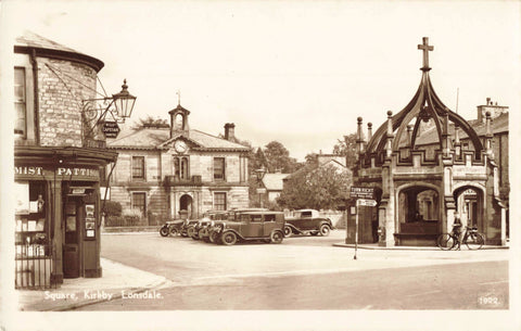 Old real photo postcard of The Square, Kirkby Lonsdale showing old cars