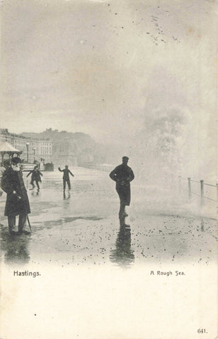 Old postcard of Hastings, showing a rough sea and people on promenade